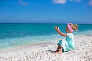 Kleines süßes Mädchen macht ein Foto am Telefon am tropischen Strand