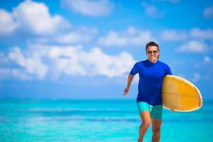 glücklicher junger Surfer, der mit einem Surfbrett am Strand läuft foto