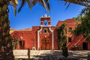 rote wände der spanischen katholischen kapelle mit palmen, bäumen und blumen, arequipa, peru foto