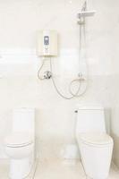 Badezimmer Interieur mit Dusche. Warmwasserbereiter und Toilette auf weißer Fliesenwand foto