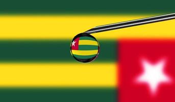 Impfstoffspritze mit Tropfen auf der Nadel vor dem Hintergrund der Nationalflagge von Togo. medizinisches Konzept Impfung. coronavirus sars-cov-2 pandemieschutz. Nationale Sicherheitsidee. foto