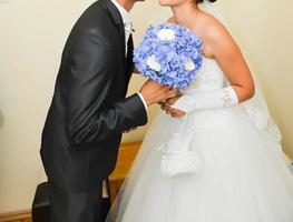 braut und bräutigam küssen sich vor der hochzeitszeremonie. Die Braut hält einen blauen Blumenstrauß foto