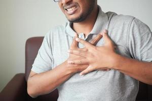 junger Mann, der Schmerzen im Herzen leidet und Brust mit Hand hält foto