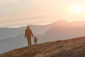 Mann, der mit seinem Hund in den Bergen spazieren geht foto