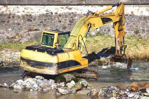 Ein Bagger, der in einem Fluss zwischen Steinen und Wasser arbeitet foto