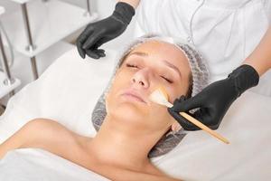 Kosmetikerin trägt Honigmaske auf das Gesicht der Frau auf, um die Gesichtshaut im Beauty-Spa-Salon mit Feuchtigkeit zu versorgen foto
