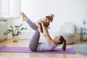 junge frau passte mutter mit babymädchen, das zu hause fitness auf der matte macht foto