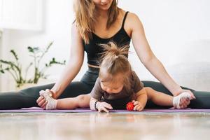 junge frau passte mutter mit babymädchen, das zu hause fitness auf der matte macht foto