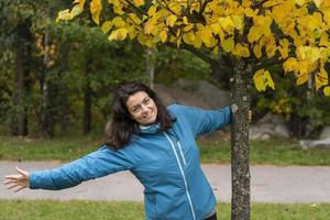 Porträt eines schönen Mädchens mit langen dunklen Haaren in einer Sportjacke neben einem bunten gelben Baum foto