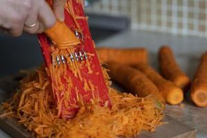 die hände der gastgeberin reiben karotten auf einer reibe für koreanische karotten, lebensstil, kochen, gesunde ernährung foto