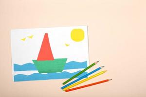 Papierhandwerk für Kinder. Anwendung der Kreativität der Kinder. Kindergarten und Handwerksschule. auf beigem hintergrund ein schiff aus farbigem papier. foto