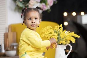 Kleines afrikanisches Mädchen sitzt in der Nähe eines Blumenstraußes und schaut in die Kamera. foto