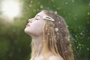 Profil eines schönen Mädchens mit langen Haaren vor dem Hintergrund von fliegenden Löwenzahnflaumen und goldenem Bokeh. foto