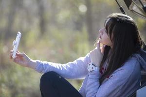 Porträt eines schönen Mädchens im Freien, das ein Smartphone benutzt, digitale Inhalte miteinander teilt und gerne ein Selfie-Foto macht. foto