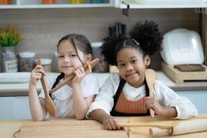 zwei glückliche kleine kinder, die zusammen kochen, teig ausrollen, an der holzarbeitsplatte in der modernen küche stehen, süß hausgemacht foto