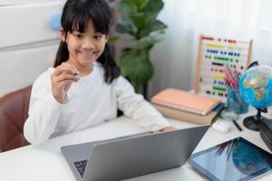 asiatische Schülerin macht ihre Hausaufgaben mit Laptop zu Hause. Kinder verwenden Gadgets zum Lernen. Bildung und Fernunterricht für Kinder. Homeschooling während der Quarantäne. Bleib zuhause foto