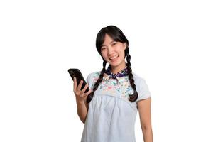Porträt einer glücklichen, schönen jungen Asiatin im Jeanskleid mit einem Smartphone auf weißem Hintergrund. Studioaufnahme foto