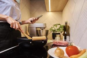 frau, die sauce bolognese kocht und smartphone verwendet foto