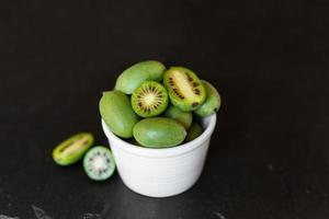 neuseeländisches exotisches essen. Beeren-Nergi oder kleine Kiwi. auf einem weißen Teller. grauer Steinhintergrund. Baby-Kiwi oder Mini-Kiwi-Früchte auf Steinhintergrund. Nahaufnahme foto