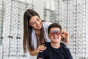 Der junge lächelnde Junge sitzt und schaut während der Sehprüfung durch die Kamera. Der Augenarzt verwendet spezielle medizinische Geräte zur Erhaltung und Verbesserung der Augengesundheit. foto