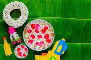 songkran festival hintergrund mit jasmingirlande, blumen in wasserschalen, duftendem wasser zum segnen und wasserpistole auf nassem bananenblatthintergrund. foto