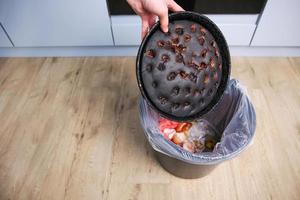 Eine Frau wirft einen verbrannten Kuchen in den Müll. foto