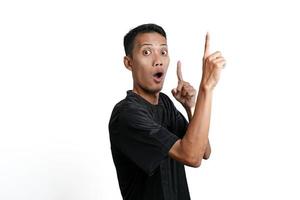 aufgeregter asiatischer mann, der schwarzes trainingst-shirt trägt und auf kopierraum zeigt. durch weißen Hintergrund isoliert foto