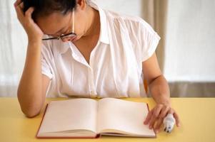 junge asiatische frau sitzt allein in ihrem zimmer, weint mit dem gesicht nach unten, während das leere buch auf den schreibtisch gelegt wird. einsamkeit, gefühl von stress und angstkonzept. foto