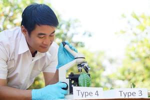 gutaussehender asiatischer naturwissenschaftslehrer experimentiert im freien, trägt blaue handschuhe, benutzt mikroskop. Konzept, naturwissenschaftliches Fach, Projektarbeit. Experiment, Bildung. Outdoor-Klasse. foto