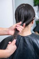 Friseur wendet eine Haarmaske auf glattes schwarzes Haar an. Haarpflege im Schönheitssalon. foto