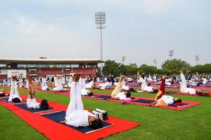 neu-delhi, indien, 21. juni 2022 - gruppen-yoga-übungssitzung für menschen im yamuna-sportkomplex in delhi am internationalen yoga-tag, große gruppe von erwachsenen, die an yoga-kursen im cricket-stadion teilnehmen foto