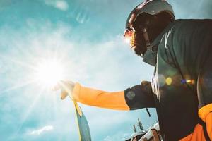 close up portrait snowboarder stand hold board blick zum himmel zur sonne schwarz copyspace mit sunburst an einem sonnigen tag. Skiurlaub foto