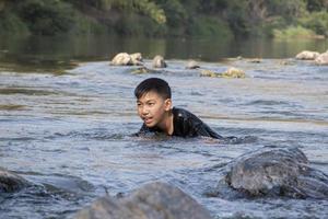 asiatische jungs verbringen ihre freizeit mit tauchen, schwimmen, steinwerfen und fischen im fluss glücklich zusammen. hobby und glück des kinderkonzepts. foto