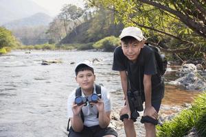 asiatische Jungen, die während des Sommercamps mit Ferngläsern Vögel auf Bäumen und Fische im Fluss im örtlichen Nationalpark beobachten, Idee zum Lernen von Kreaturen und Wildtieren und Insekten außerhalb des Klassenzimmers. foto