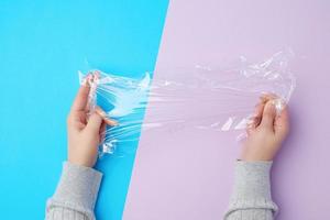 Zwei Hände halten ein Stück transparente Plastikfolie auf einem farbigen Hintergrund foto