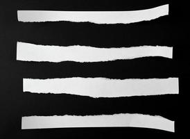 zerrissene leere weiße Papierstreifen vor schwarzem Hintergrund foto