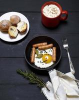 Ei mit Würstchen in einer schwarzen Bratpfanne, Kakao mit Marshmallows foto