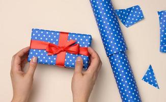 weibliche hände halten eine blaue geschenkbox auf beigem hintergrund, das konzept der glückwünsche zum geburtstag foto