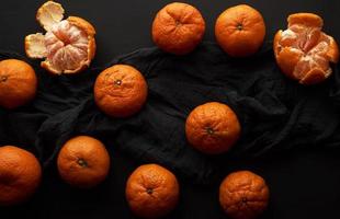 geschälte reife Orangenmandarine und ein Bündel ungeschälter runder ganzer Früchte auf einer schwarzen Serviette foto