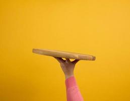 Frau, die leeres rundes Pizzabrett aus Holz in der Hand hält, Körperteil auf gelbem Hintergrund foto