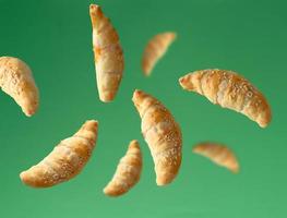 fliegende Mini-Croissants, bestreut mit Sesamsamen auf grünem Hintergrund foto