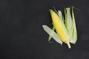 frischer Maiskolben auf einem rustikalen schwarzen Holztisch mit Kopierraum - Draufsicht foto