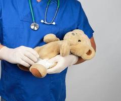 arzt in blauer uniform bandagen weißer medizinischer verband pfote brauner teddybär foto