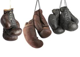 Drei Paar sehr alte Boxhandschuhe aus Vintage-Leder, die an Schnürsenkeln hängen foto