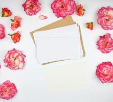 Rosa Rosenknospen und ein Umschlag aus weißem Papier auf weißem Hintergrund foto