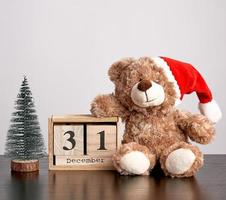 Brauner Teddybär mit rotem Hut, Tischkalender aus Holz mit dem Datum 31. Dezember foto
