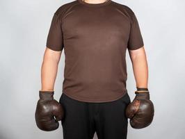Junger Mann steht mit sehr alten braunen Boxhandschuhen an den Händen foto