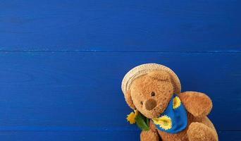 beiger Teddybär, der auf einem blauen Holzhintergrund sitzt foto