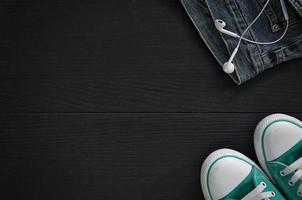 paar turnschuhe, ein fragment von jeans und kopfhörern auf schwarzem holzhintergrund foto