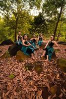 eine gruppe asiatischer frauen macht urlaub im wald, während sie einen grünen rock tragen und auf einem felsen sitzen foto